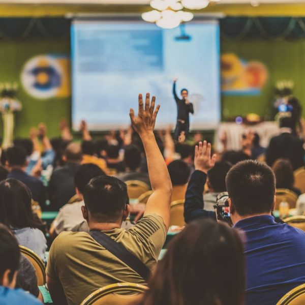 rear-view-of-audience-showing-hand-to-answer-the-question-from-speaker-on-the-stage.jpg